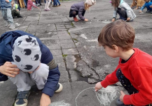 Dzieci rysują kolorowymi kredami na betonie.